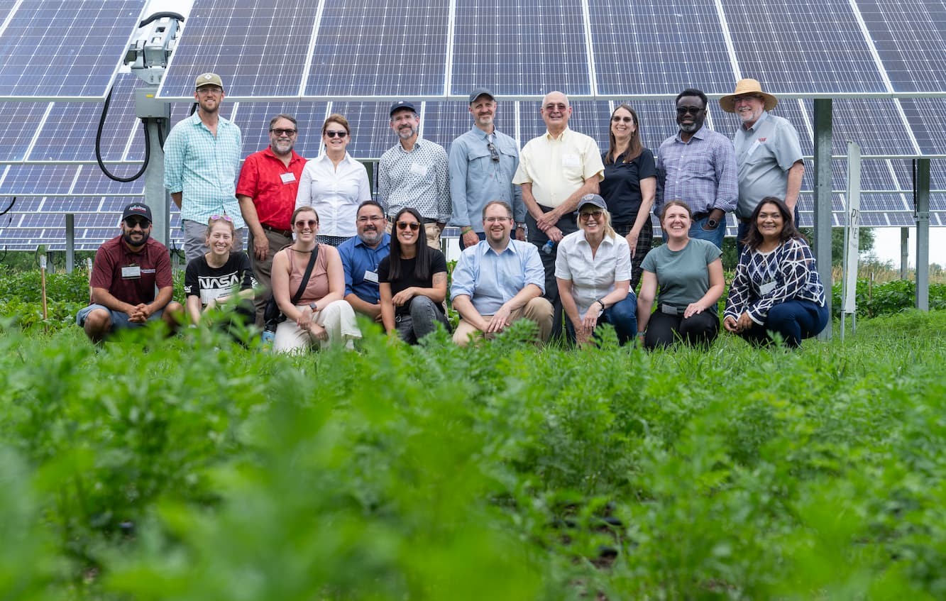 A group of people posing for a photograph in a field in front of a PV solar array.